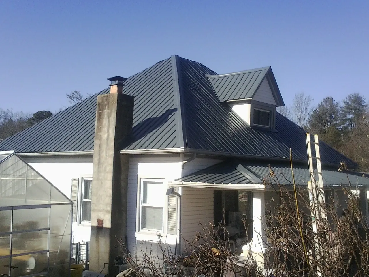 Dark blue standing seam metal roof on a white farmhouse with dormer — Slate & Tile Roof Repair by Roofing Brothers in Hartsel