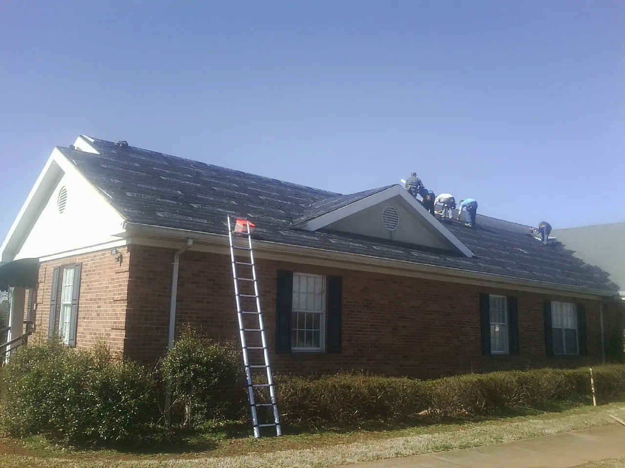 Crew tearing shingles off a brick ranch roof with a ladder set — Emergency Roof Repair work by our crew in Hartsel