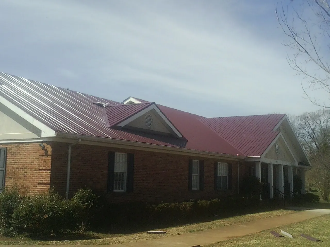 Red metal roof with gabled entries on a long brick building, from a Hail Damage Roof Repair job in Hartsel