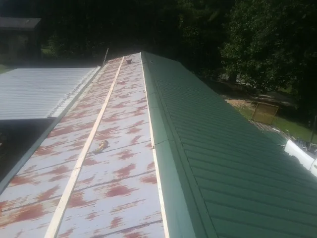 Old rusted panels beside newly installed green metal roofing — Wind Damage Roof Repair by Roofing Brothers in Hartsel