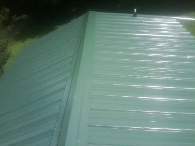 New green metal panels meeting at the ridge of a roof — Flat Roof Repair work by our crew in Hartsel