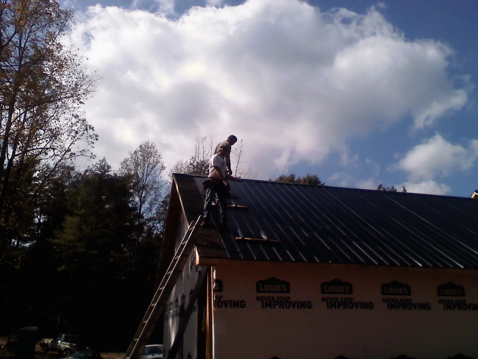 Roofer fastening dark metal panels high against a cloudy sky, from a Roof Inspection job in Hartsel