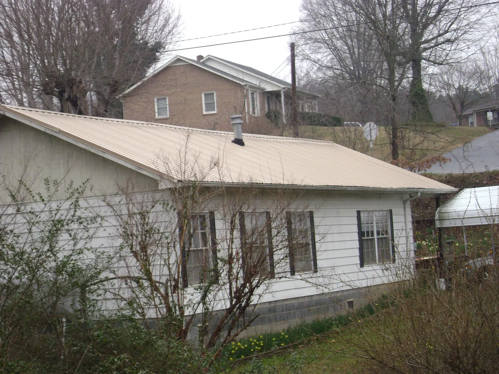 Tan metal roof on a white sided house set into a hillside — Commercial Roofing by Roofing Brothers in Hartsel