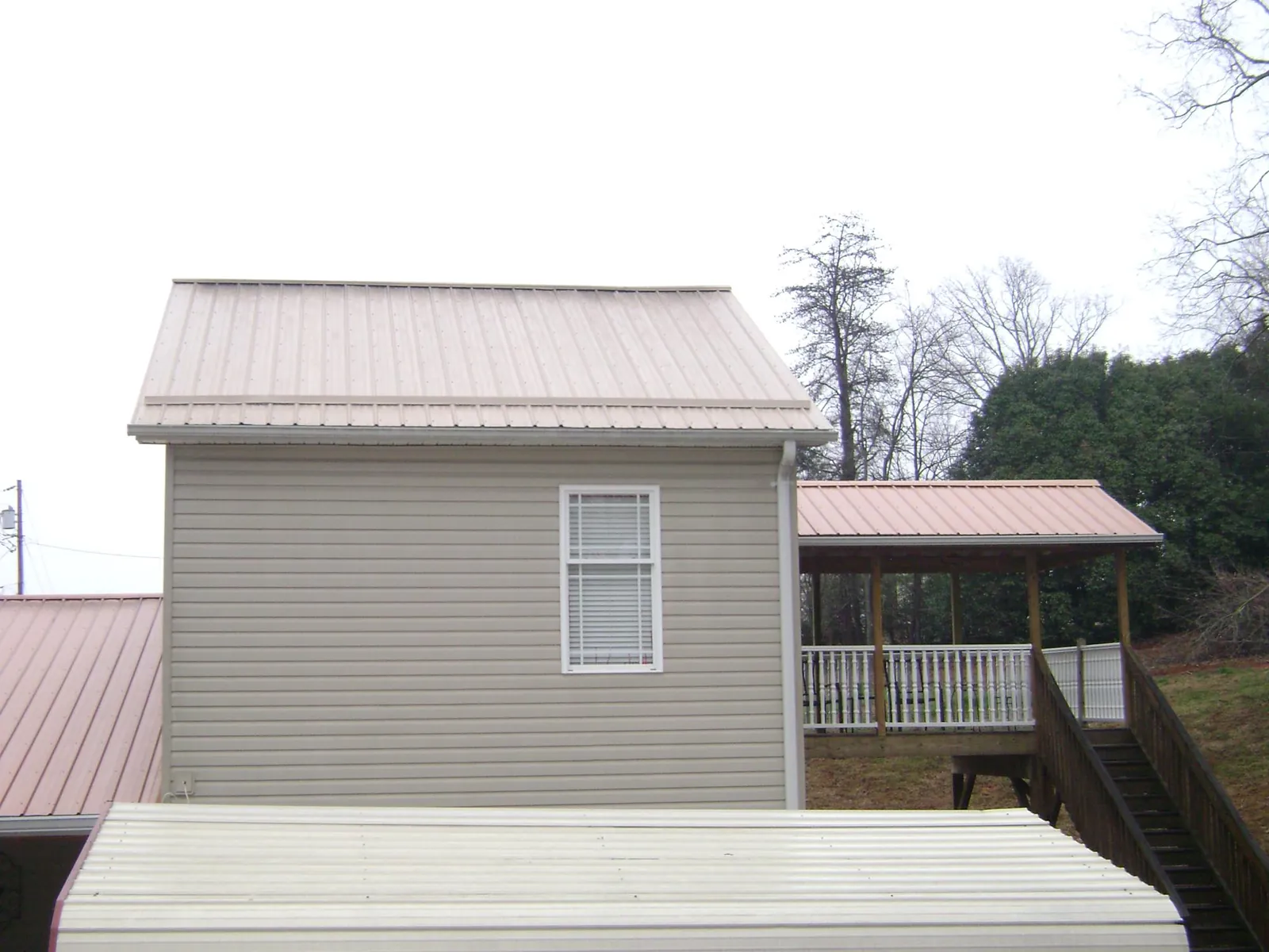 Tan metal roofs on a two story addition and attached porch, from a Roof Replacement job in Hartsel